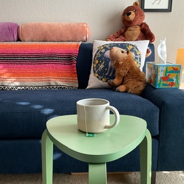 A photo of a cup of tea sitting on a small coffee table in front of a large couch.