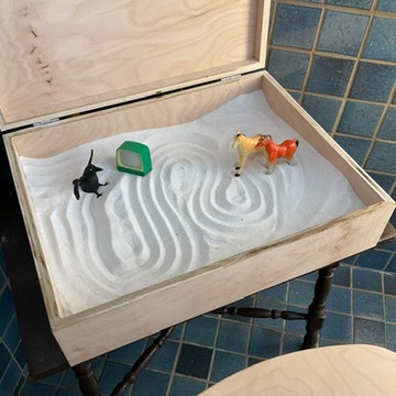 A photo of a small toy crow and two small toy horses in a sand tray